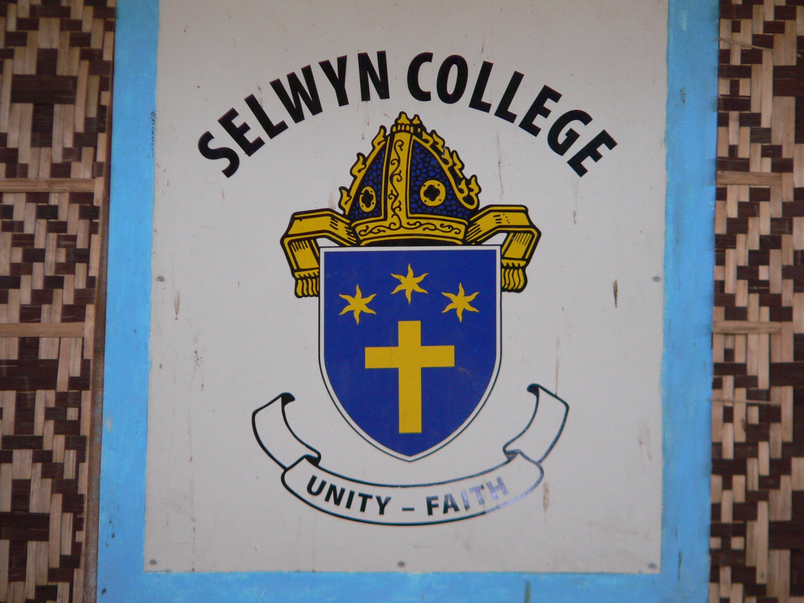 Logo of Selwyn College, a showing a shield with three stars, a cross and a bishops' hat